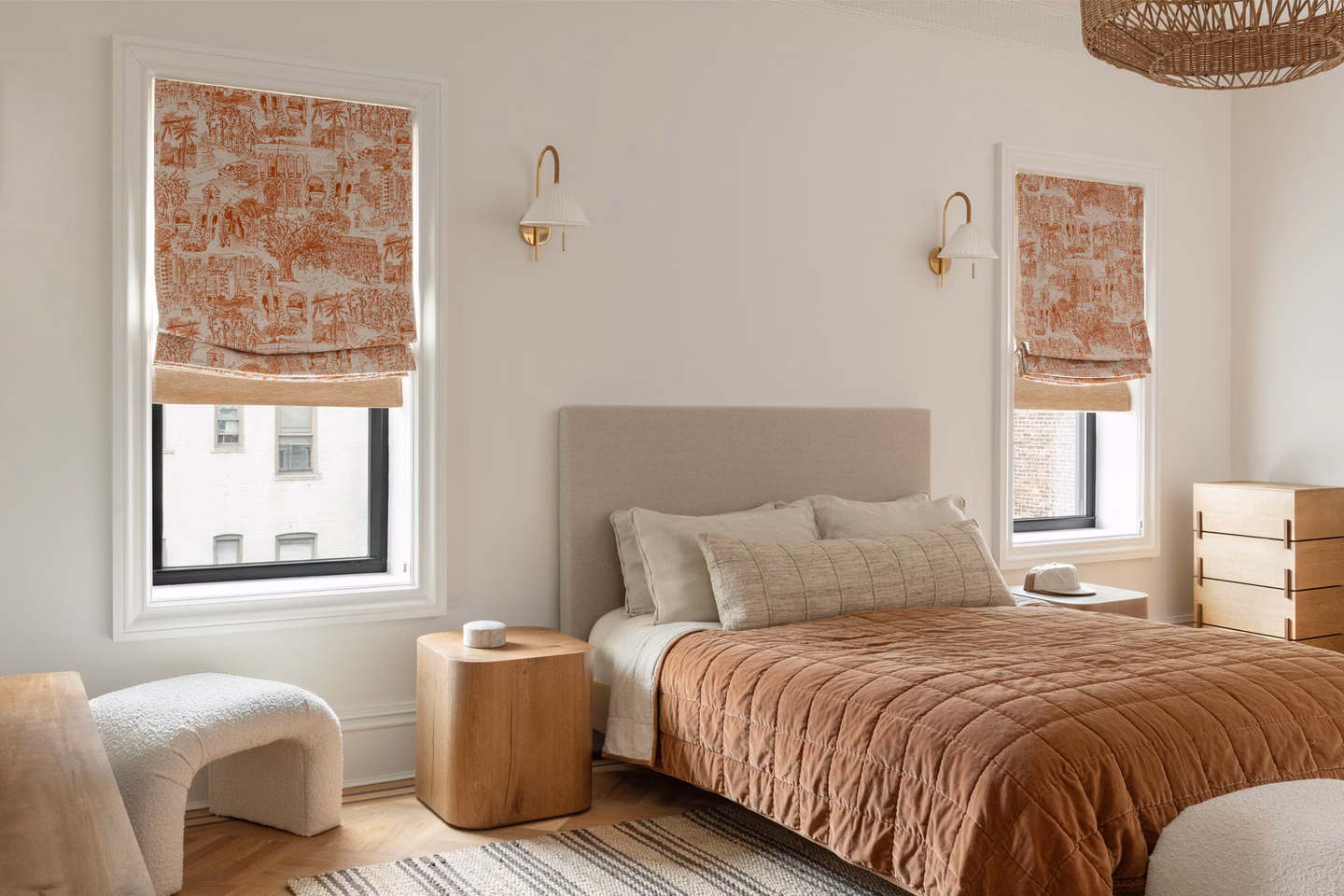 Custom French printed linen relaxed Roman shades paired with woven wood shades in a warm, neutral bedroom