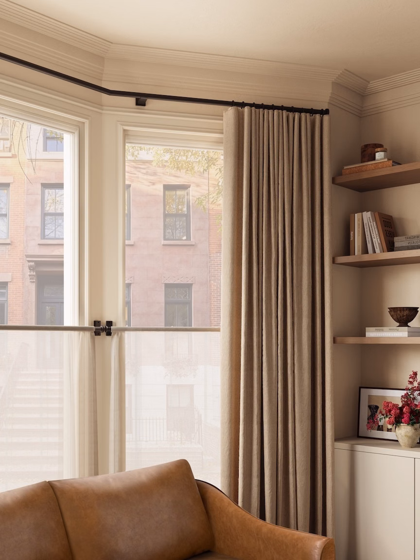 Heavy linen drapes in Neutral frames a corner living room window over European style cafe curtain.