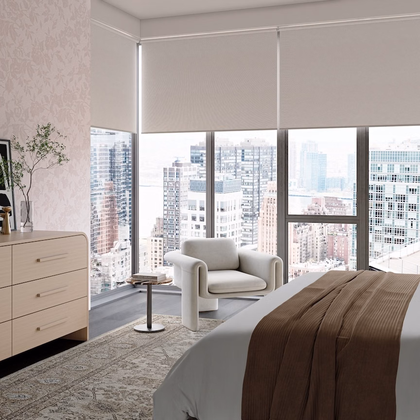 Feather white blackout roller shades cover corner windows in a modern high-rise bedroom overlooking the city.