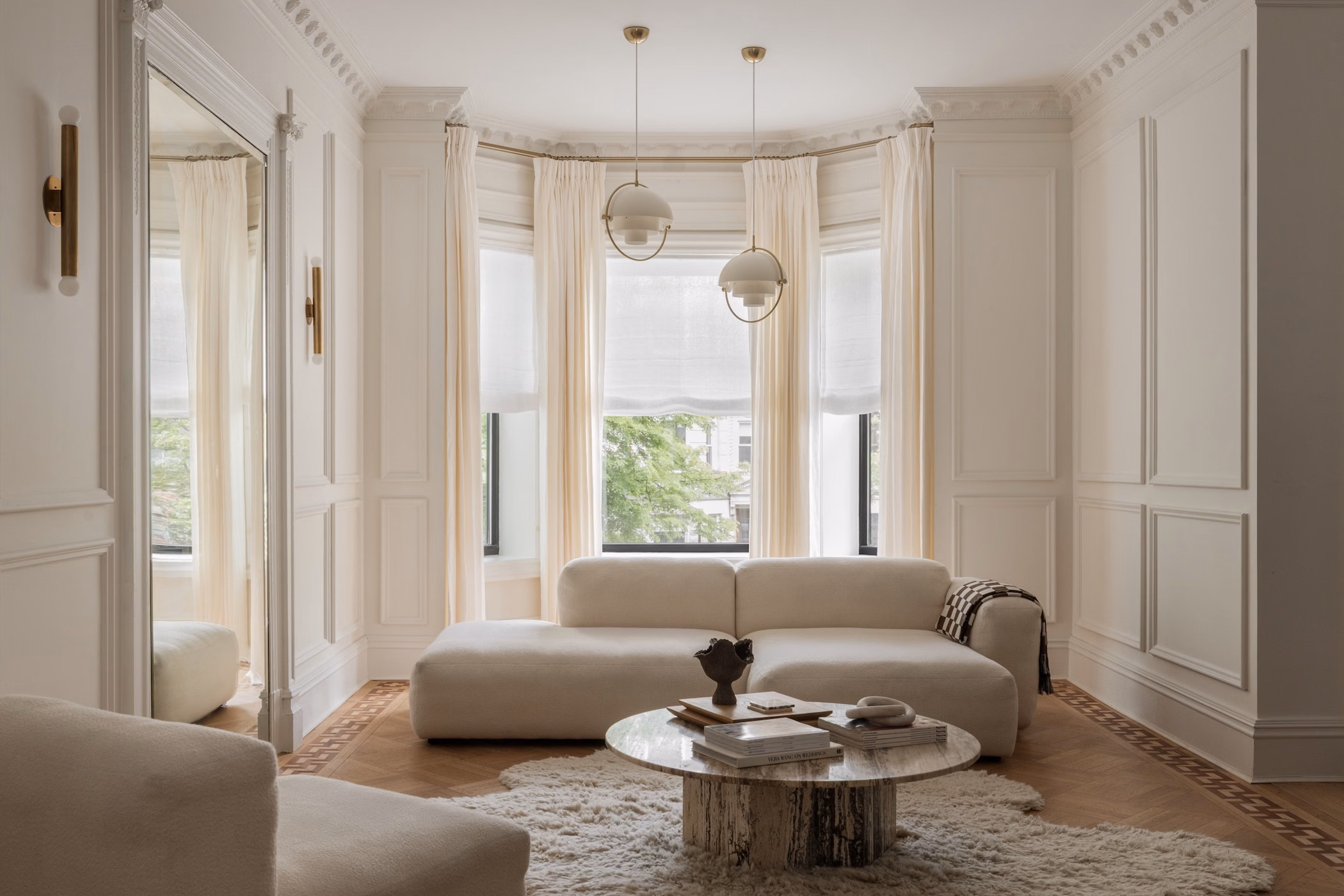 Sheer linen relaxed Roman shades soften a curved bay window in an elegant neutral living room.