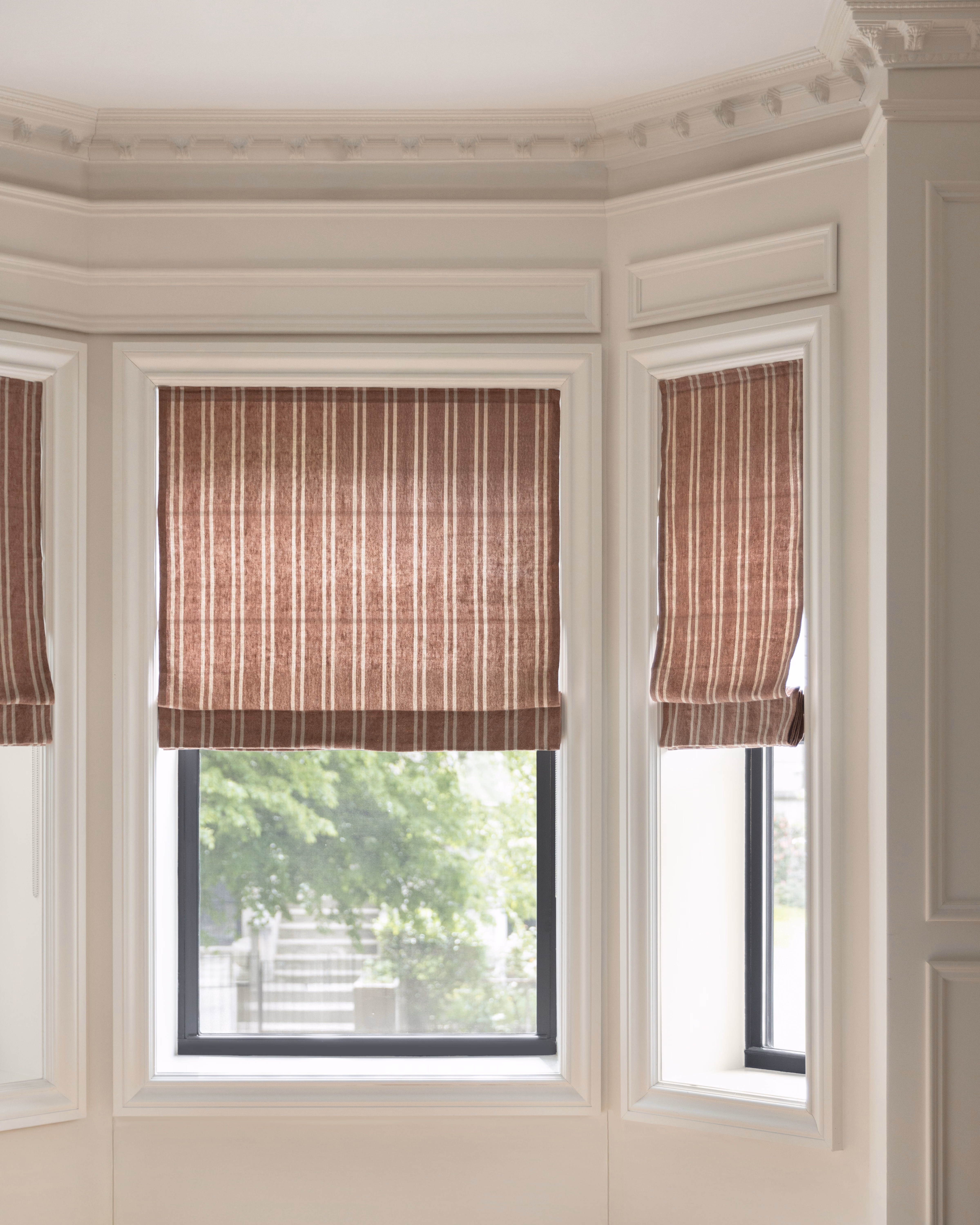 Terracotta striped unlined linen flat Roman shades add warm pattern to a bright bay window.