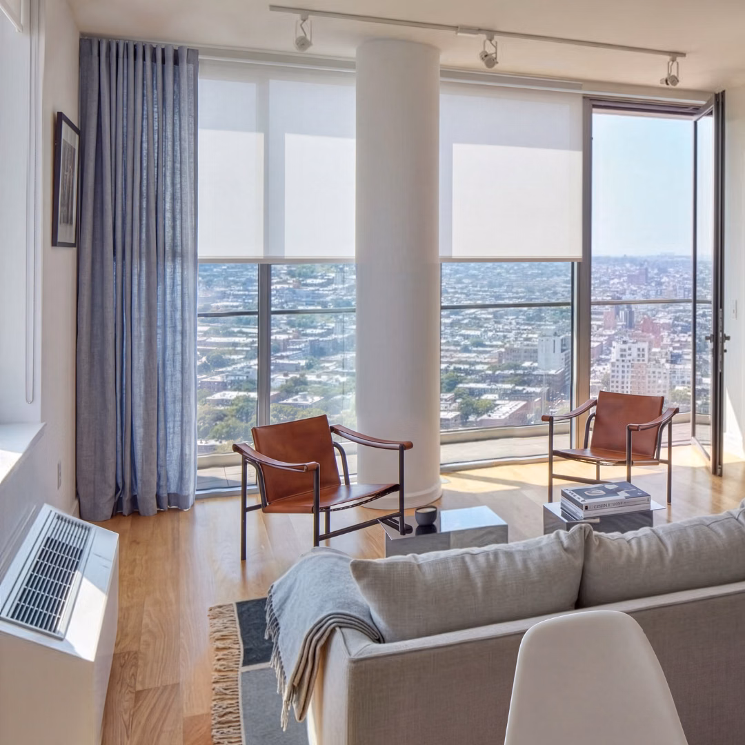 Sheer linen drapes frame floor-to-ceiling windows with city views in a modern high-rise living room.